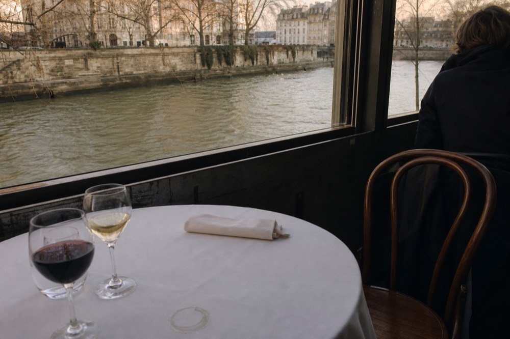 Table setting on a Seine dinner cruise with wine glasses and a view of the river, no text, no logos, no people