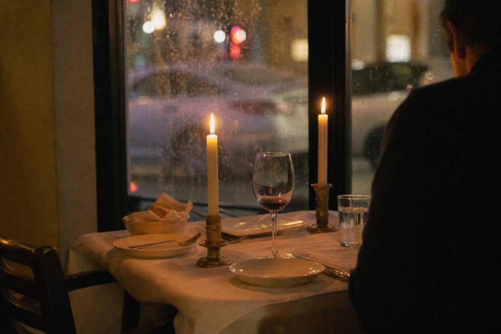 Couple at a candlelit dinner table aboard a Seine cruise boat with Paris lights outside the window, no text, no logos, no people