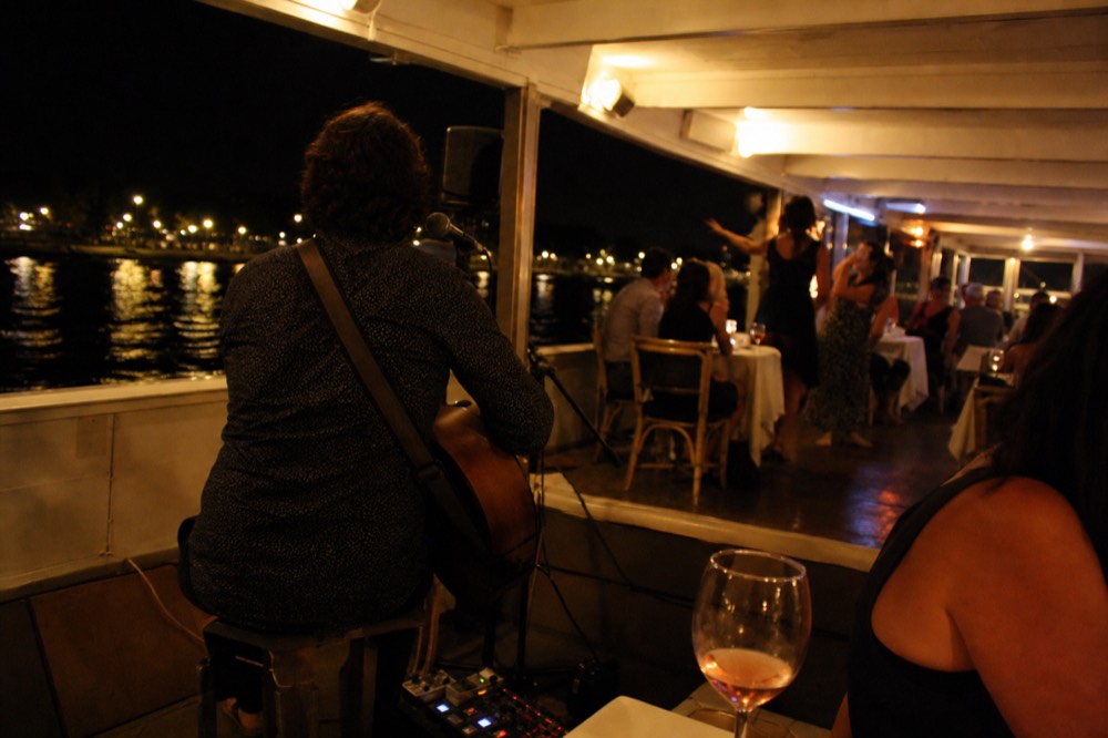 A musician performing near tables of diners on a large illuminated river boat, no text, no logos, no people
