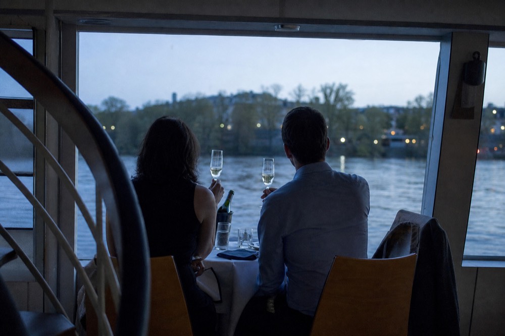 A couple toasting with champagne at a small window-side table on a quiet boat, no text, no logos, no people