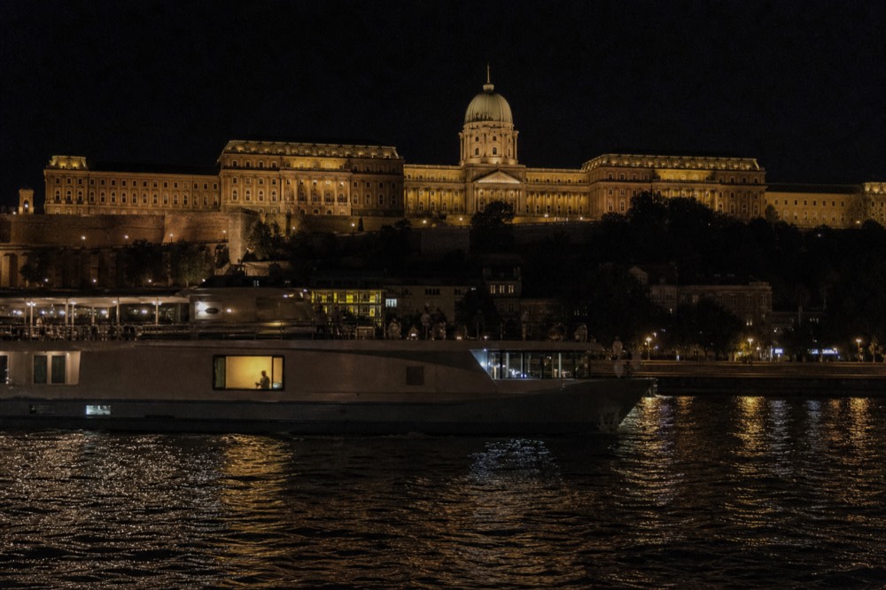 A dinner cruise boat gliding past the illuminated Louvre on the Seine at night, no text, no logos, no people