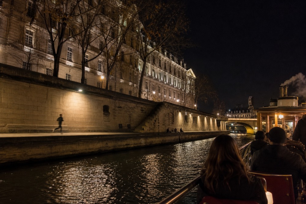 Dinner cruise boat passing the illuminated Louvre and its riverside quay at night, no text, no logos, no people
