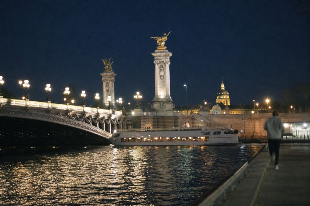 Dinner cruise boat lit from within cruising past illuminated Paris architecture on the Seine at night, no text, no logos, no people