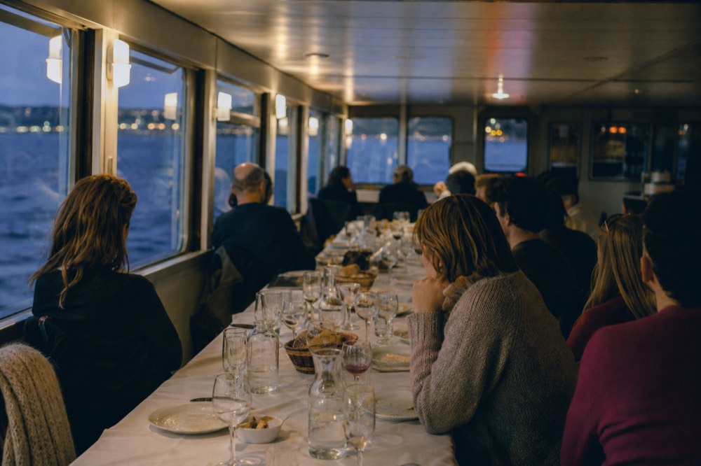 A long shared dinner table set for a group aboard a boat, glasses and bread baskets on the table, no text, no logos, no people