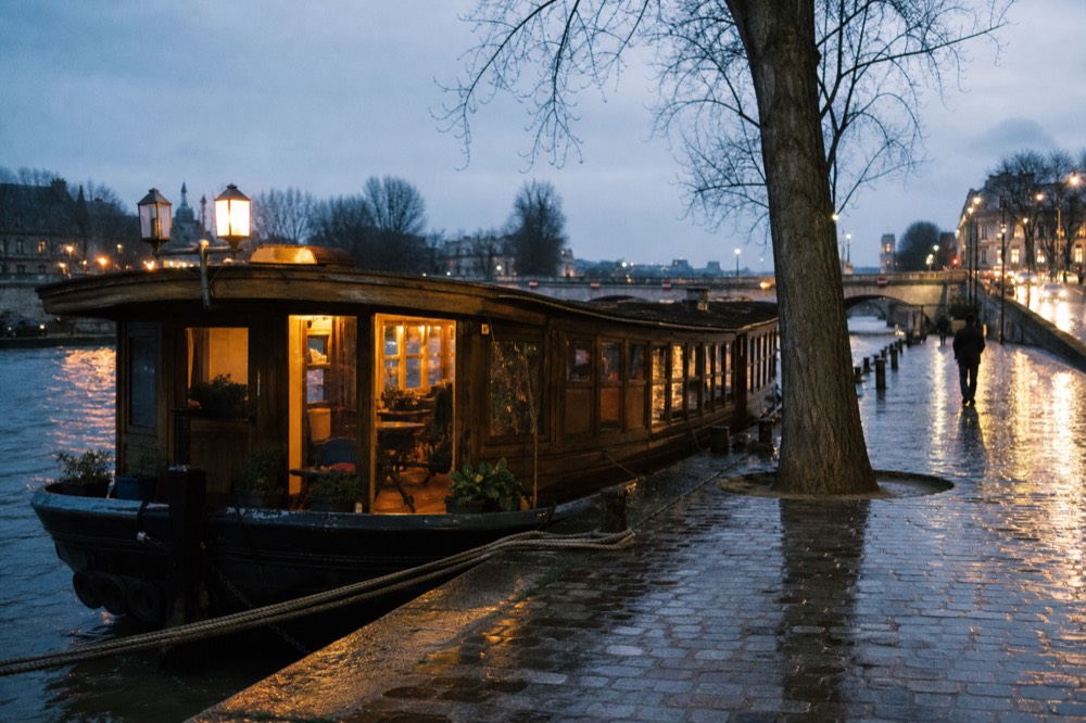 A vintage wooden barge with warm interior lighting moored on the Seine at dusk, no text, no logos, no people