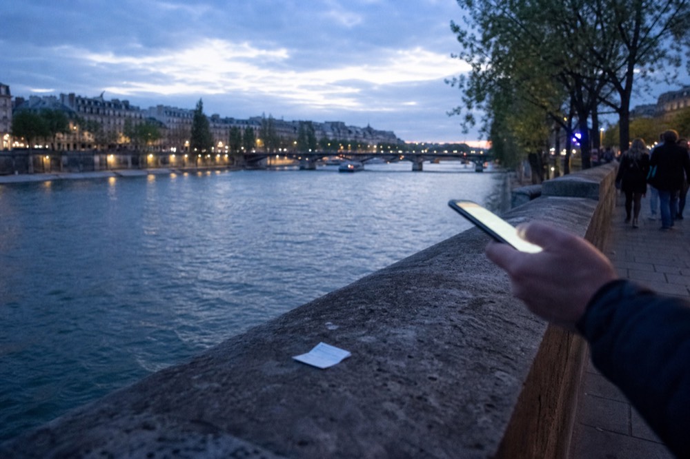 A confirmation email on a phone held over a Paris riverbank at evening, no text, no logos, no people