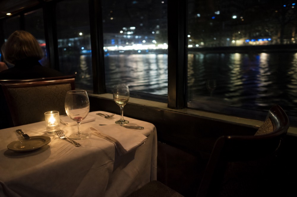 Candlelit dining table set with wine glasses aboard a Seine river boat, no text, no logos, no people.