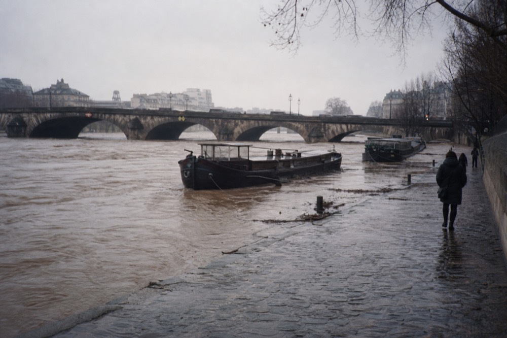 A high, fast-flowing Seine river with moored boats near a Paris bridge, no text, no logos, no people.